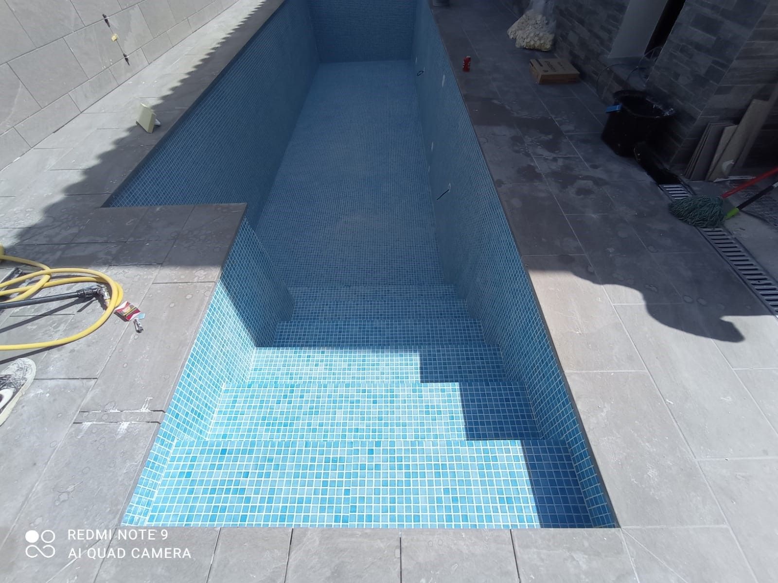 Canal de nado alargado revestido de gresite azul claro con escalera de obra, antes del llenado