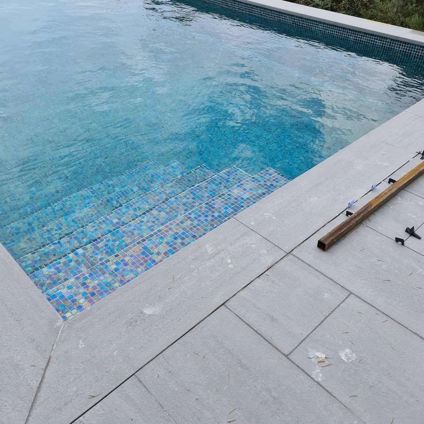 Detalle de gresite irisado en tonos azules junto a la coronación de una piscina