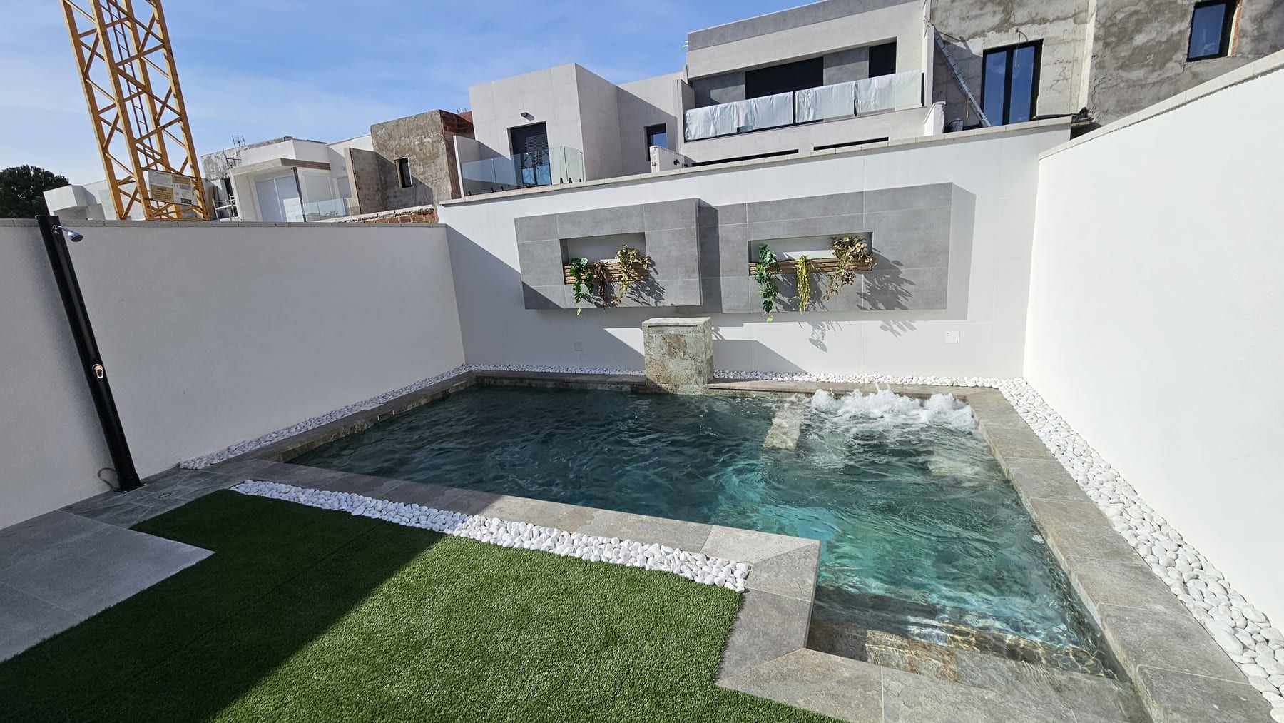 Piscina con cascada y muro blanco con jardineras, con la cascada y las jardineras