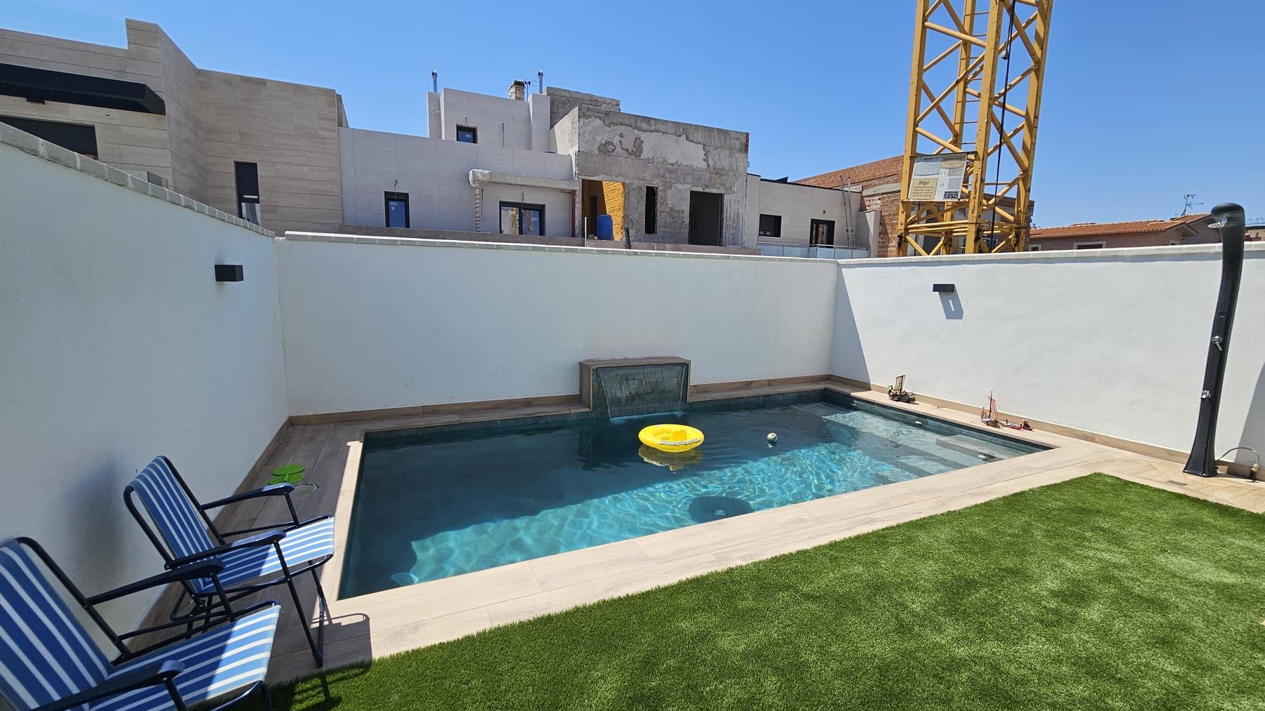 Piscina con cascada en patio blanco, con la cascada de lámina