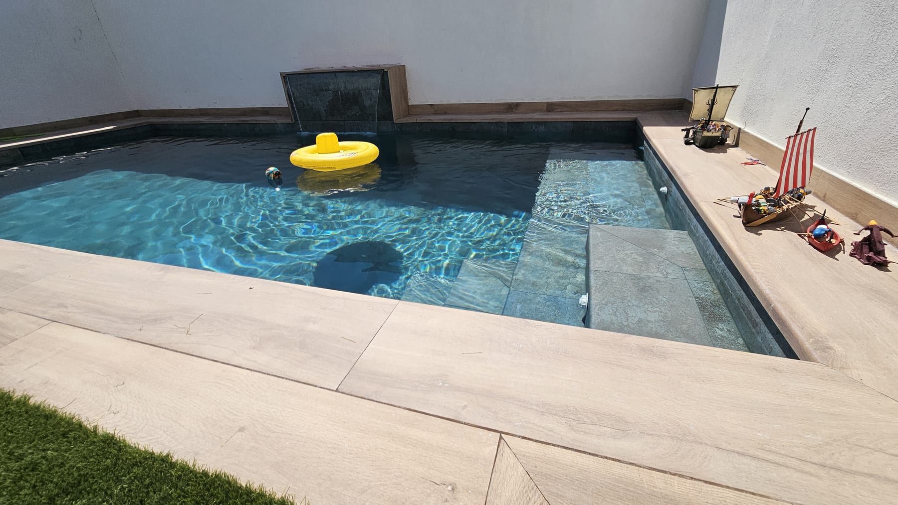 Piscina con cascada en patio blanco, con el banco interior