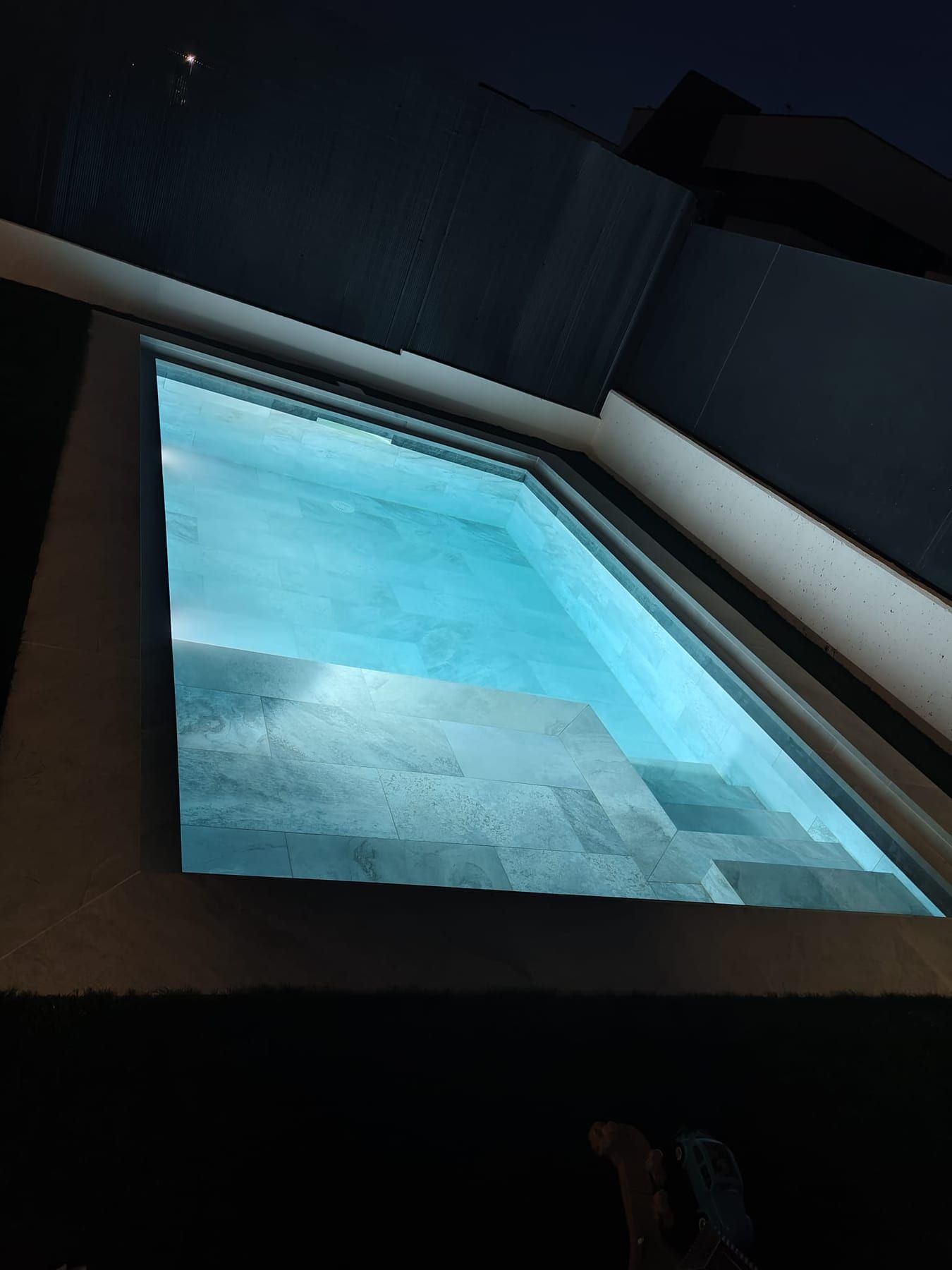 Piscina cuadrada de porcelánico gris con iluminación, iluminada al anochecer