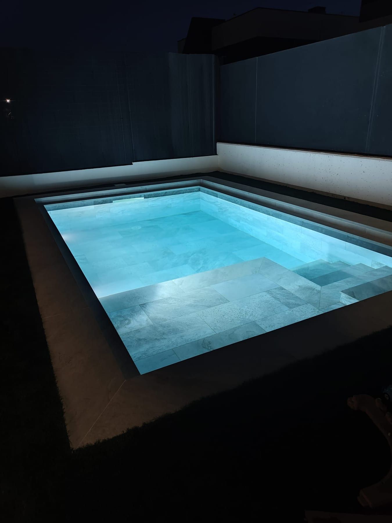 Piscina cuadrada de porcelánico gris con iluminación, iluminada al anochecer
