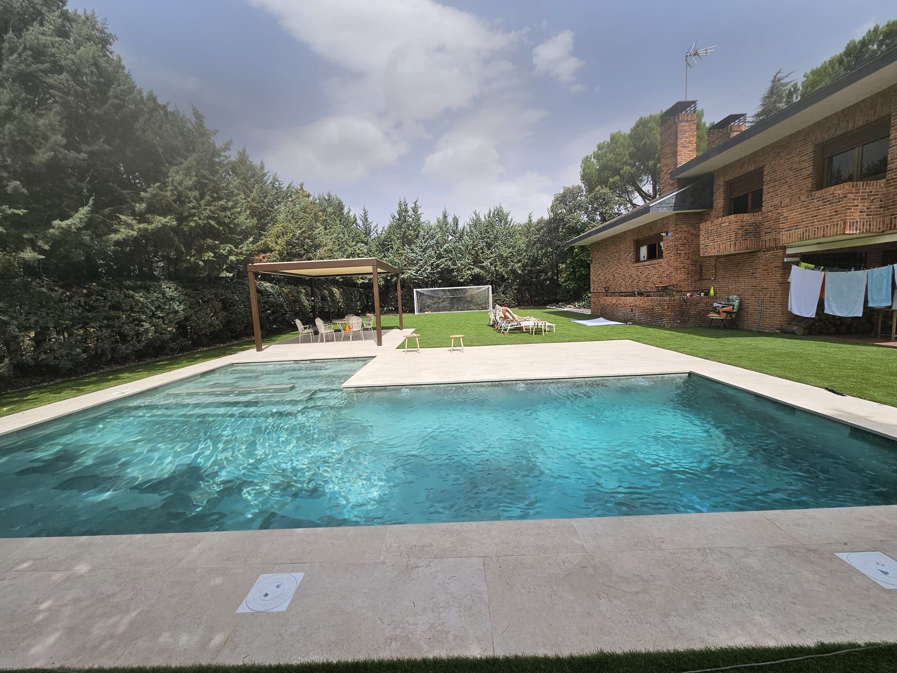 Piscina en L con gran playa en jardín amplio, junto al chalet y la pérgola