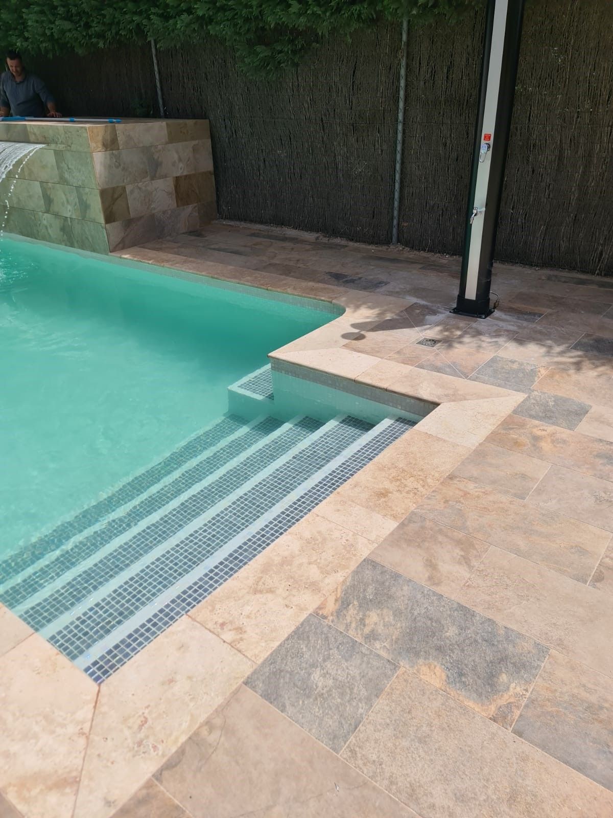 Piscina con escalera de obra y coronación de piedra travertino integrada en el pavimento exterior