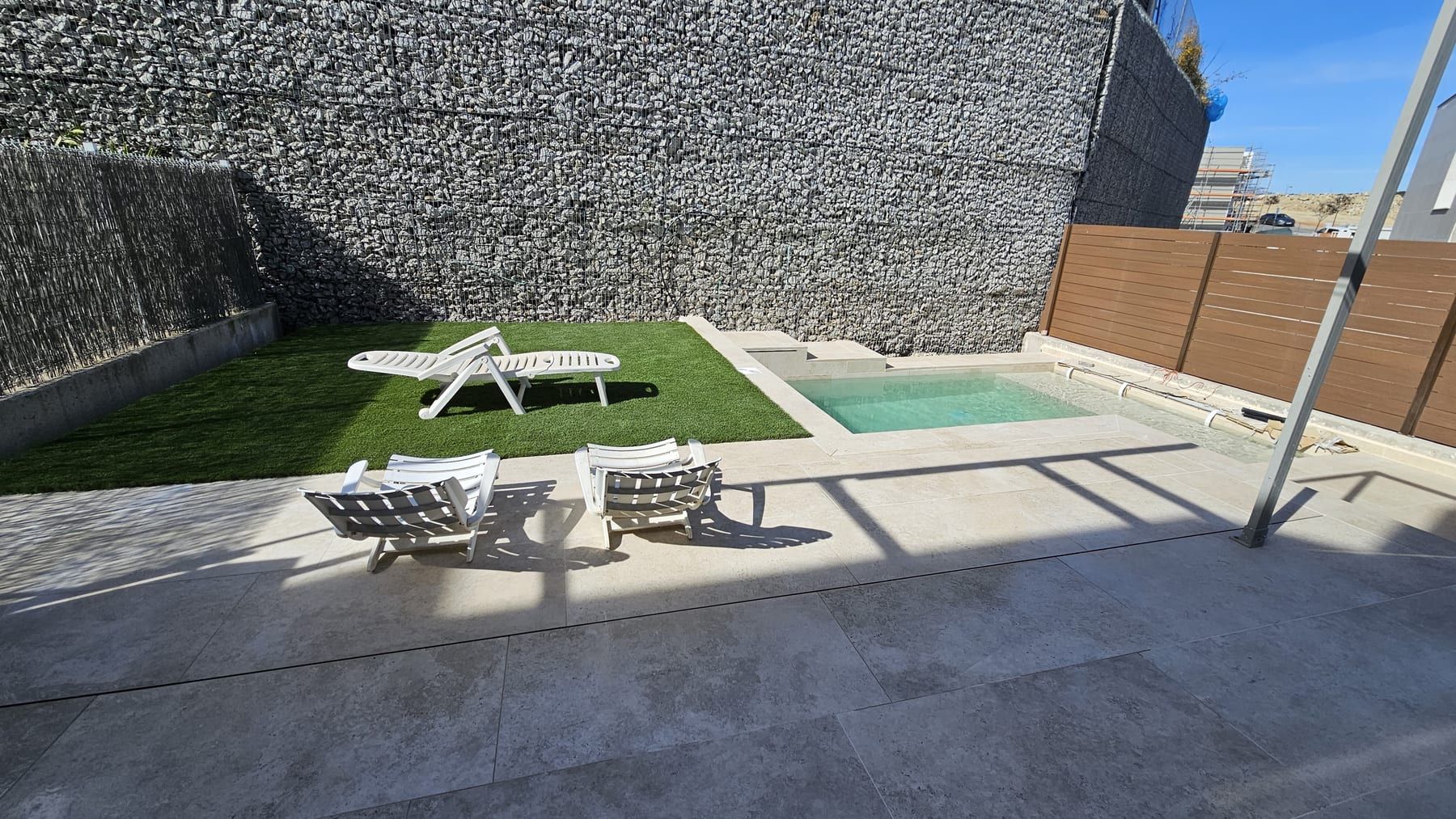 Piscina con escalera y playa junto a muro de piedra, vista 2