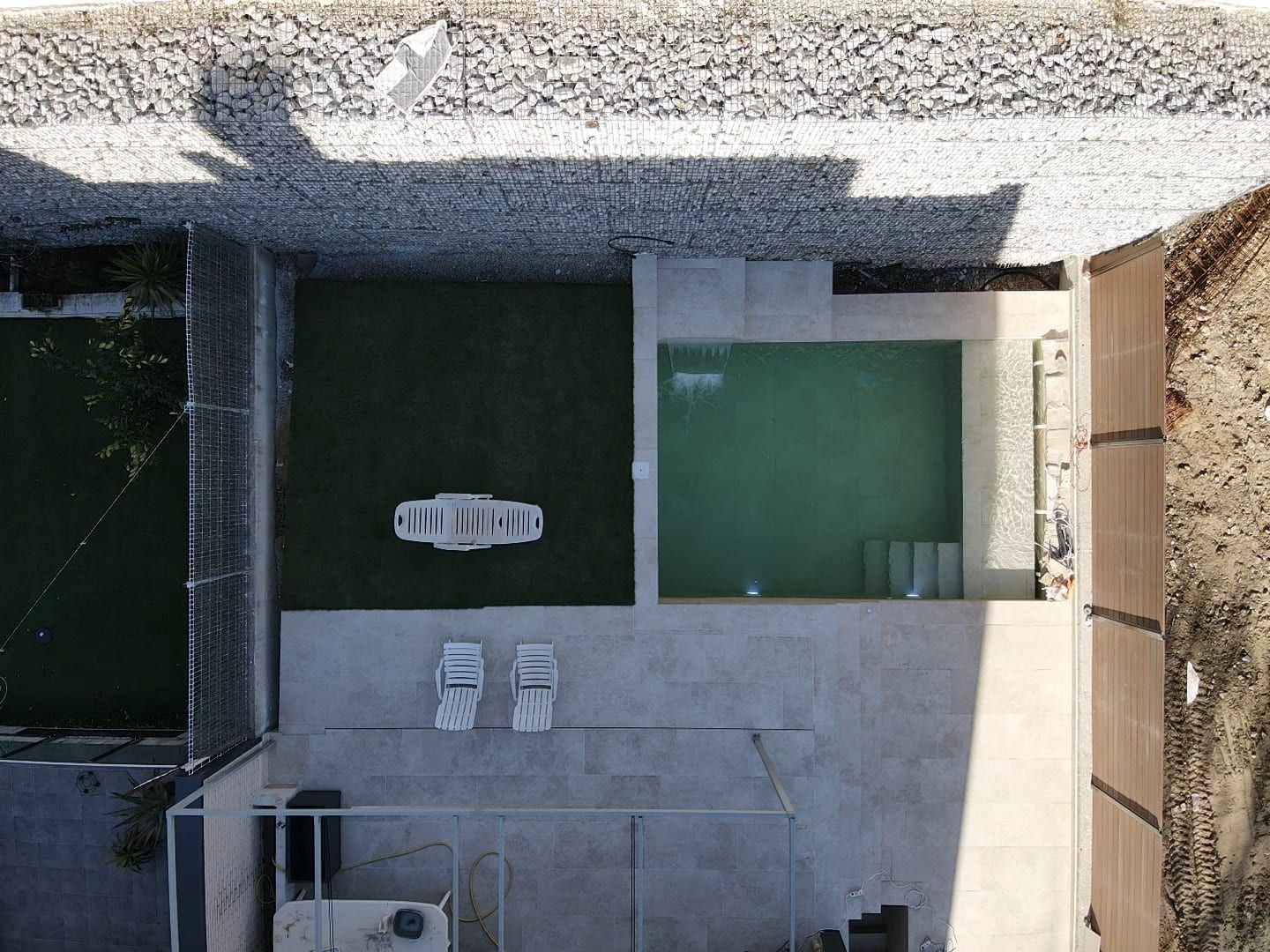 Piscina con escalera y playa junto a muro de piedra, vista cenital con dron