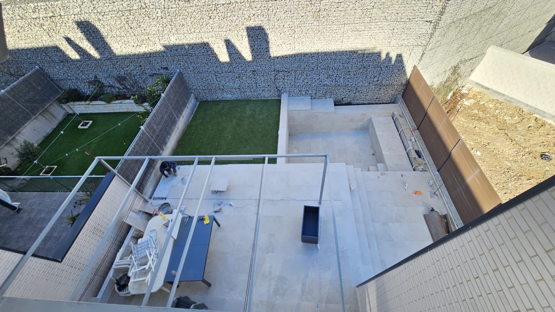 Piscina con escalera y playa junto a muro de piedra, durante la obra