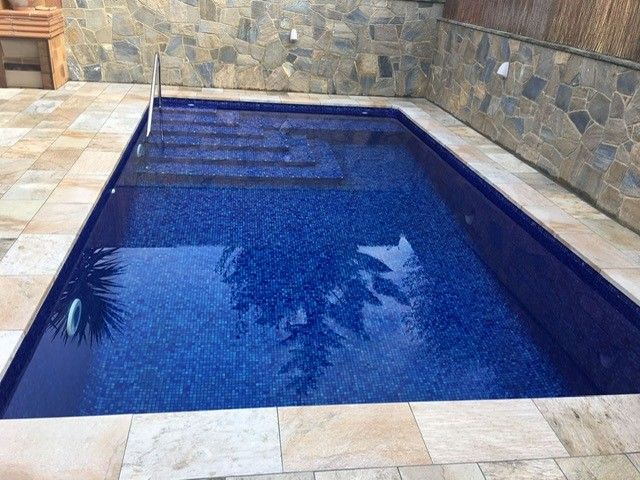 Piscina con gresite azul oscuro y muro de piedra al fondo