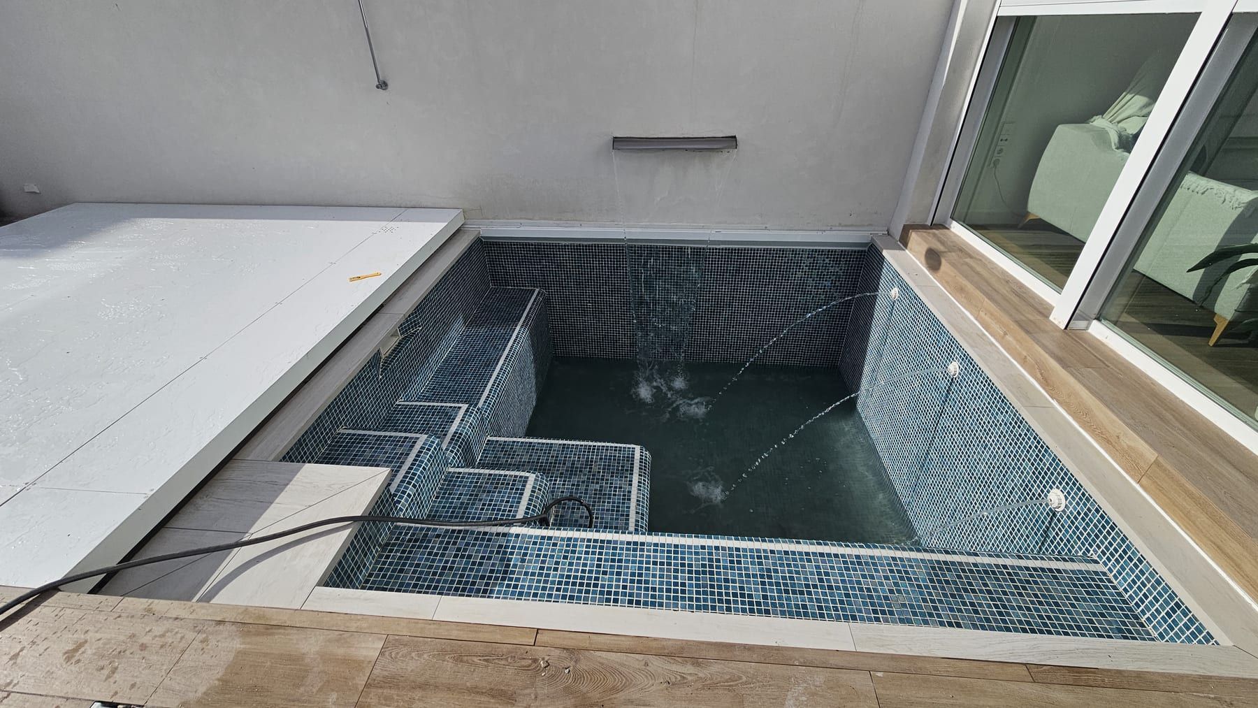Piscina de gresite oscuro con escalera de obra en patio