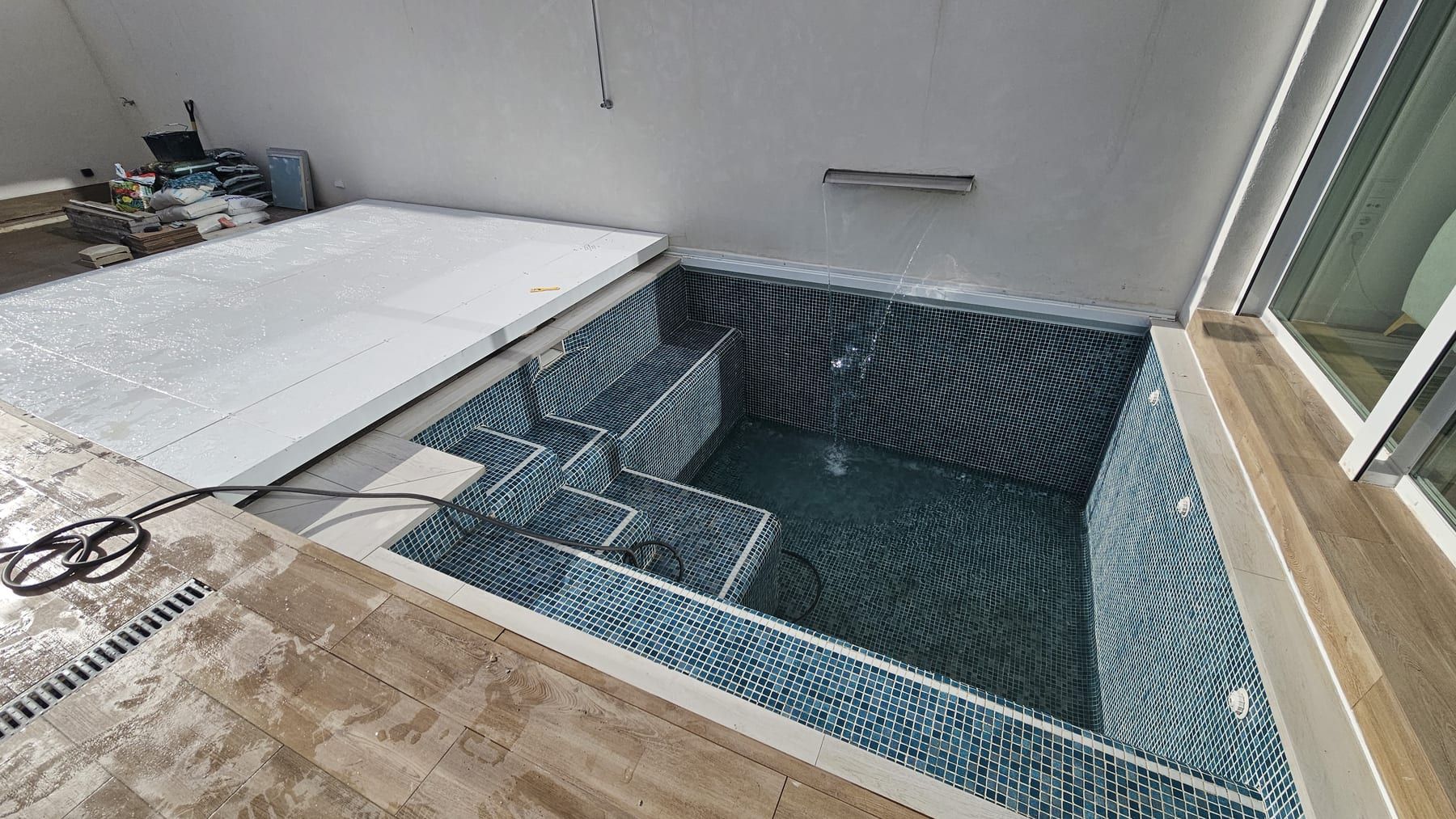Piscina de gresite oscuro con escalera de obra en patio, con la escalera de obra