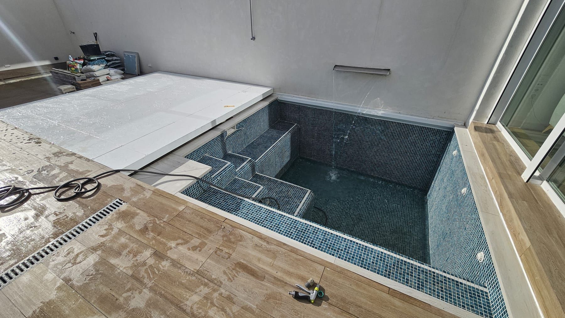 Piscina de gresite oscuro con escalera de obra en patio, vista 3