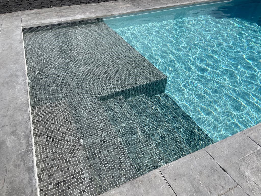 Detalle de piscina con gresite gris verdoso y banco de obra sumergido junto a la coronación