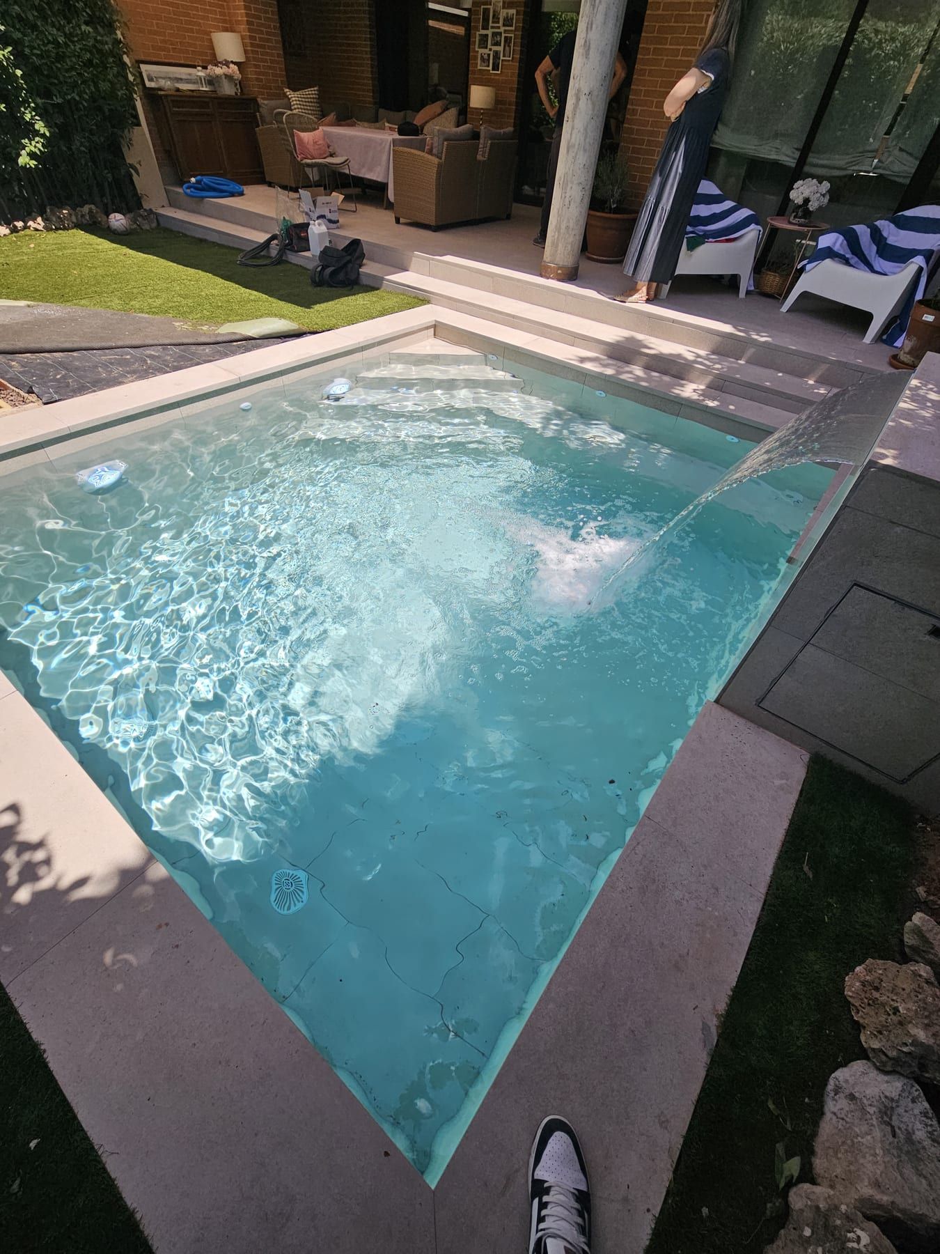 Piscina en tonos gris verdoso con chorro de pared, con el chorro de pared en funcionamiento