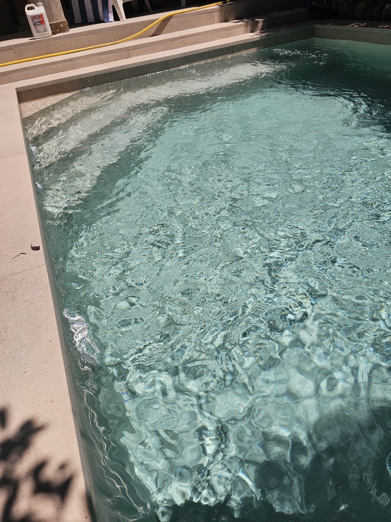 Piscina en tonos gris verdoso con chorro de pared, detalle del revestimiento