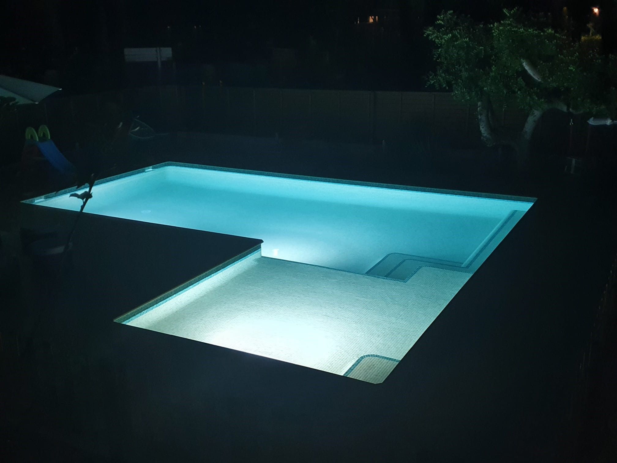 Piscina de obra iluminada de noche con focos LED que tiñen el agua de azul turquesa