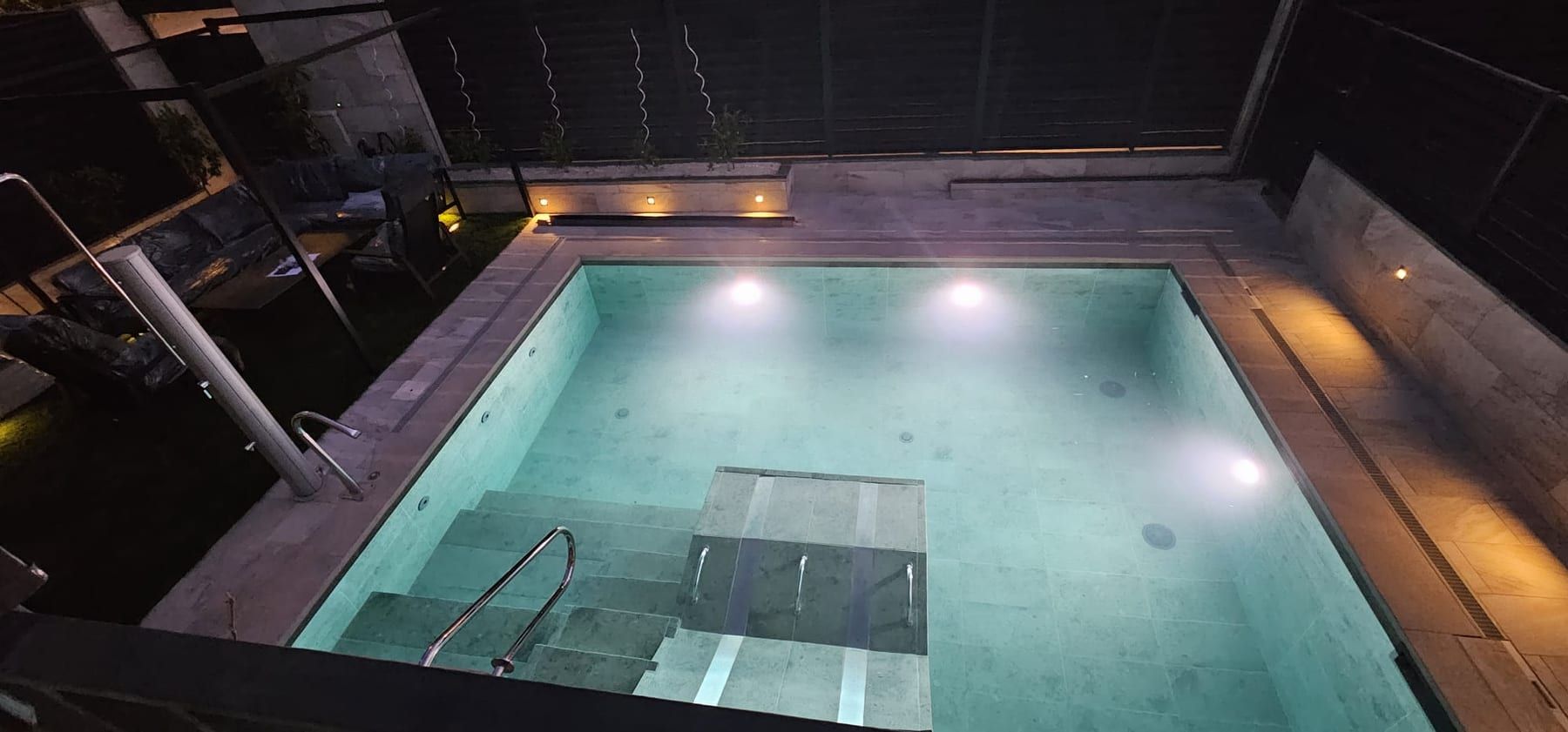Piscina iluminada con escalera y banco de hidromasaje, iluminada de noche
