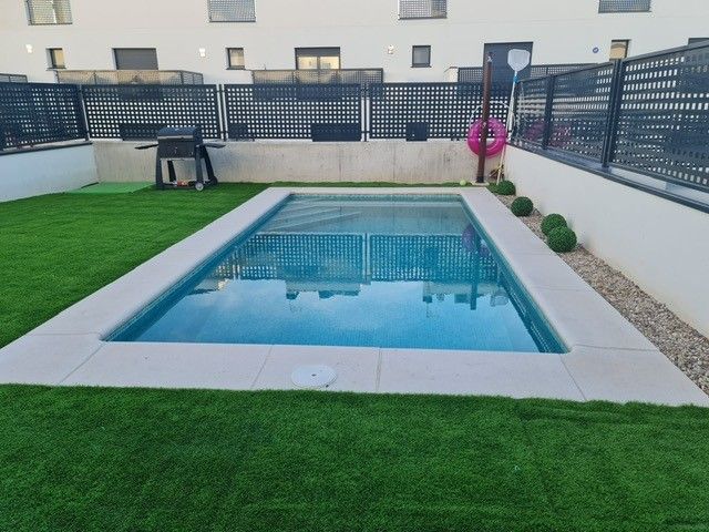 Piscina compacta de obra con coronación clara en un jardín con césped y valla
