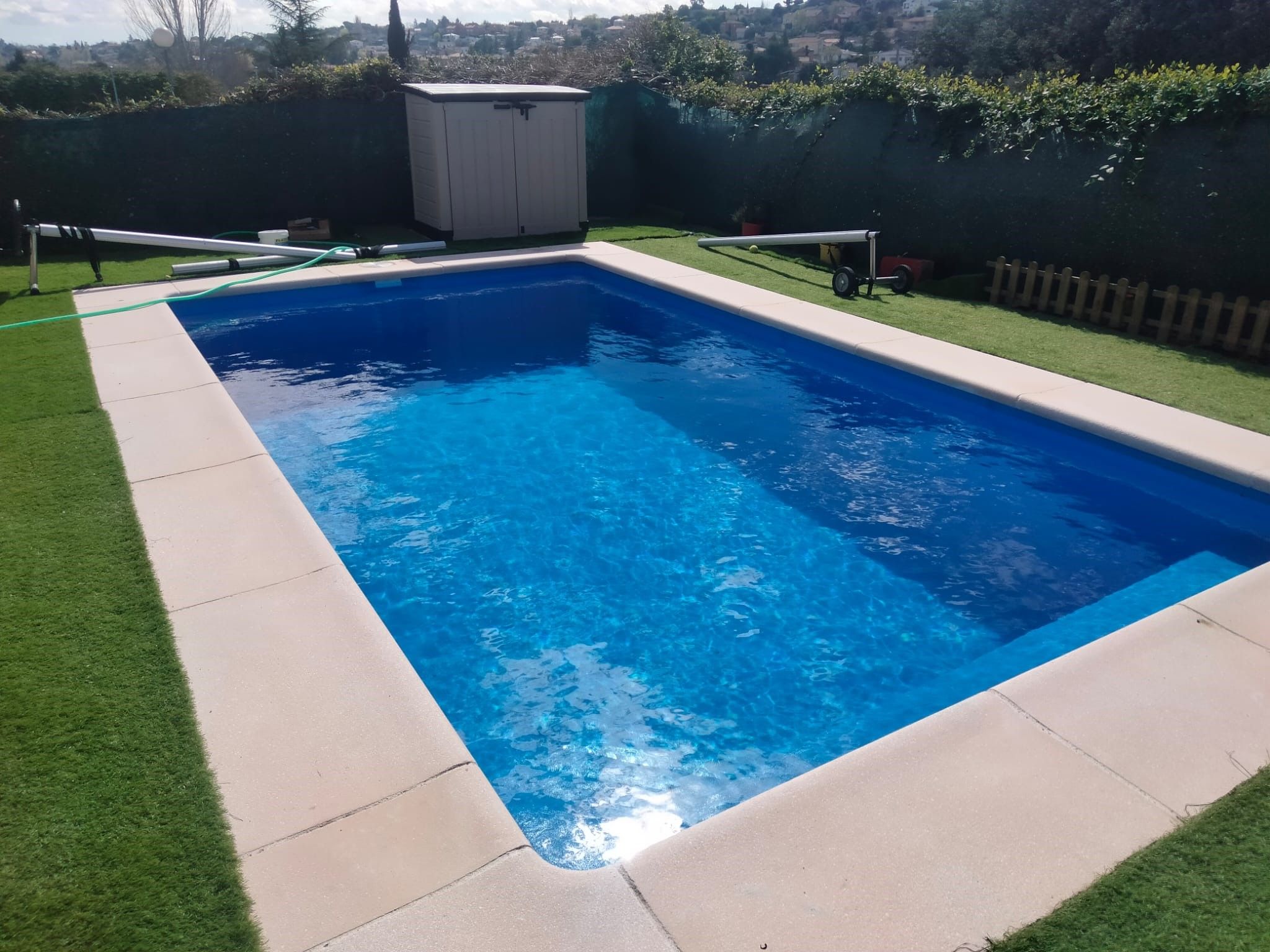 Piscina de obra rectangular revestida de gresite azul, con coronación clara y césped alrededor