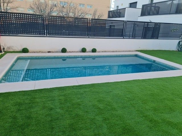 Piscina pequeña de obra con coronación clara rodeada de césped artificial
