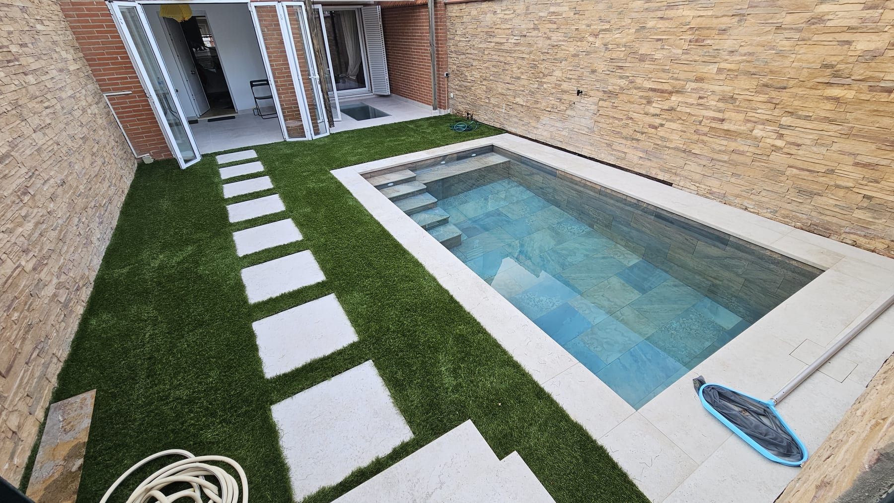 Piscina pequeña con escalera y paso de losas sobre césped, con el camino de losas