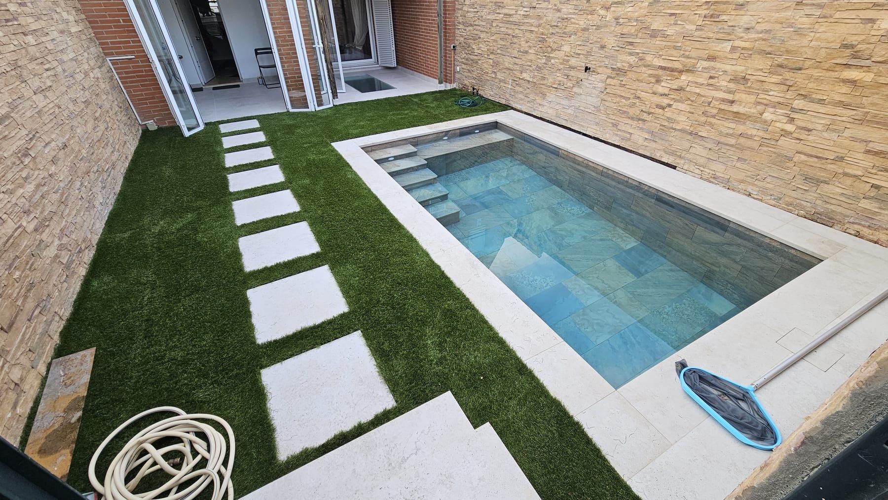 Piscina pequeña con escalera y paso de losas sobre césped, vista 2