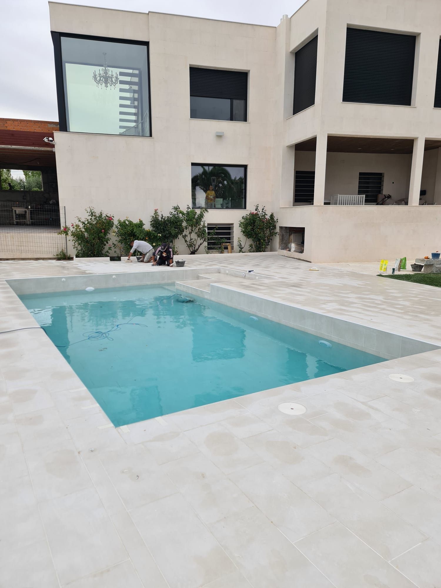 Piscina rectangular revestida de porcelánico beige con coronación y solado a juego junto a una vivienda