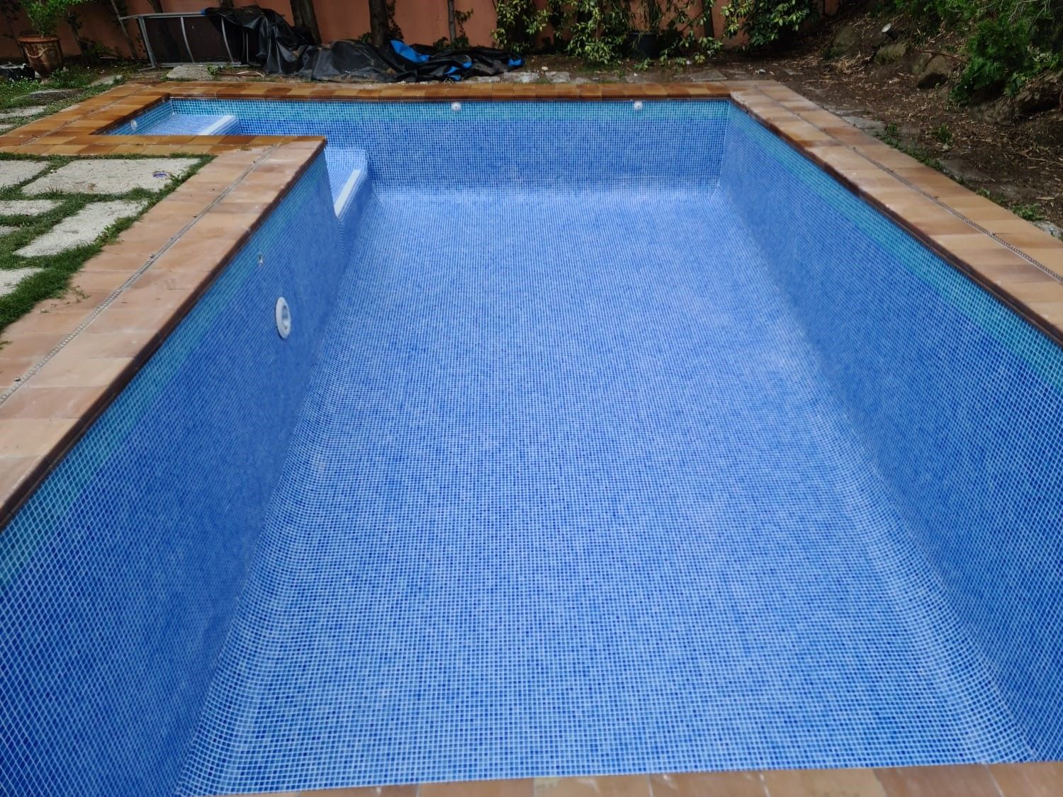 Vaso de piscina vacío recién revestido de gresite azul, con escalera de obra en una esquina