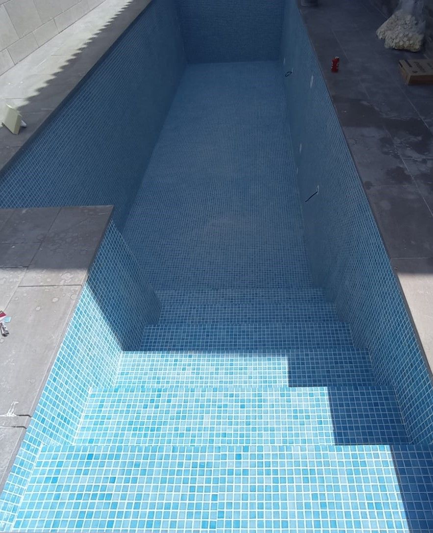 Vaso de piscina revestido de gresite azul claro con escalera de obra en esquina, antes del llenado